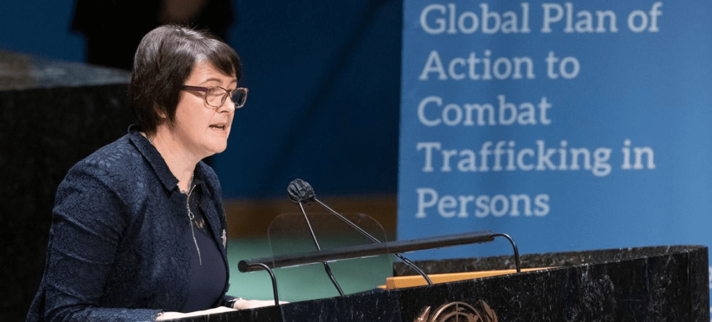 A speaker delivers a speech at a podium with a United Nations emblem, discussing the Global Plan of Action to Combat Trafficking in Persons.